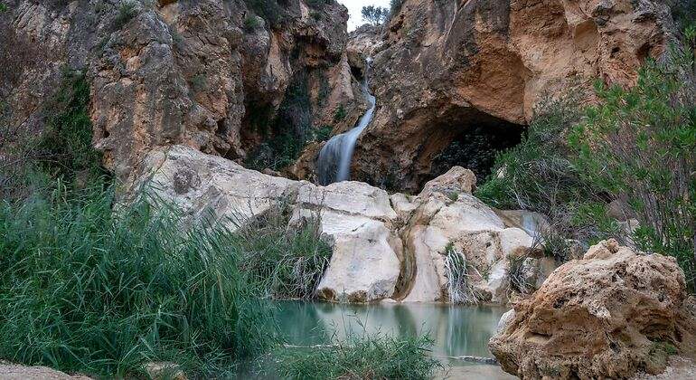 Hermoso paisaje en larga exposición con agua sedosa de una cascada en la cueva de las Palomas rodeada de vegetación y rocas en Buñol, Valencia, España