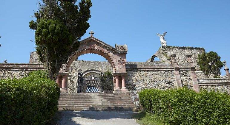 Entrada de arco de piedra al cementerio de Comillas en el que en uno de los mausoleos se puede ver la estatua de un ángel