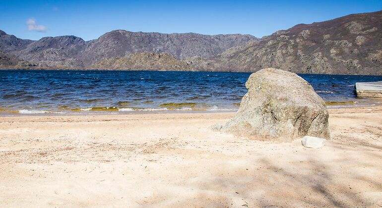 Playa de arena en un lago con un pedrusco en medio del arenal