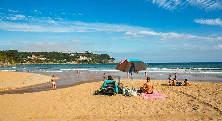 Playa de Asturias con arenas doradas y gente tomando el sol y jugando en la orilla
