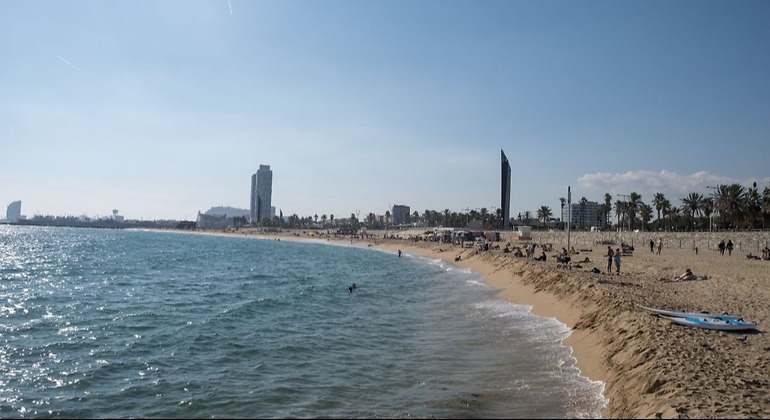 Zona de playa con algunos bañistas y las torres de la Barceloneta al fondo