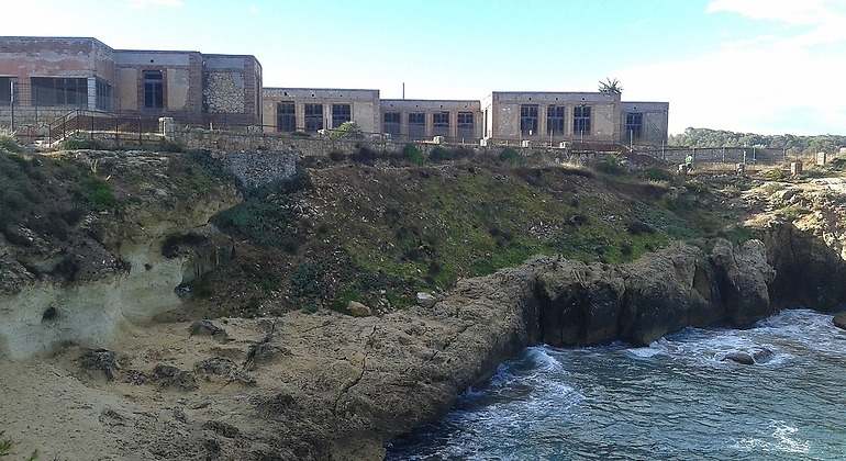 Una construcción que parece medio derruida sobre un acantilado con el mar rompiendo en él.