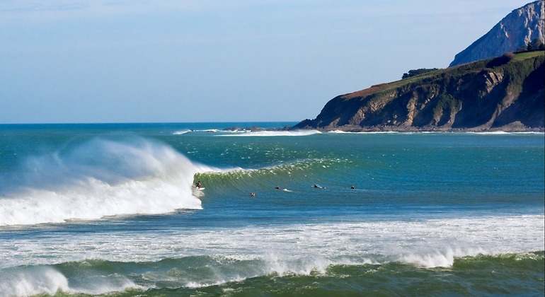 Surfistas en Mundaka con un peñón sobresaliendo al fondo