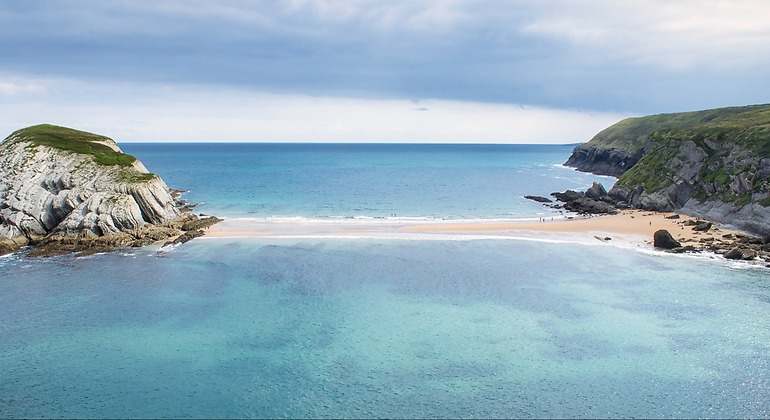 Tómbolo de arena que une la isla del Castro con la costa cantábrica durante la merea baja en Covachos