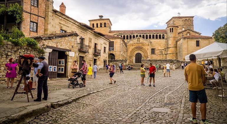 Plaza Mayor de Santillana del Mar con turistas paseando de día y la Colegiata de Santa Juliana al fondo