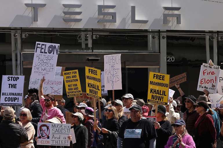Personas participan en una concentración de protesta contra Elon Musk frente a una sala de exposición de Tesla en el Third Street Promenade de Santa Mónica