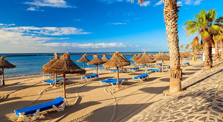 Una playa de arenas doradas en la que hay un mar de aguas cristalinas y muchas tumbonas y sombrillas para los turistas