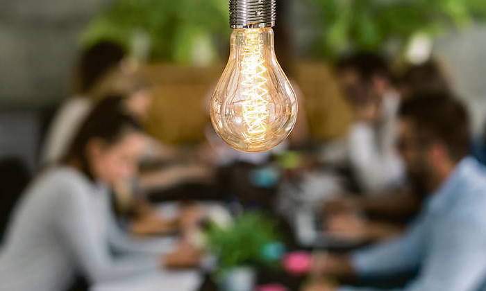 Varias personas trabajan y piensan ideas bajo una bombilla iluminada
