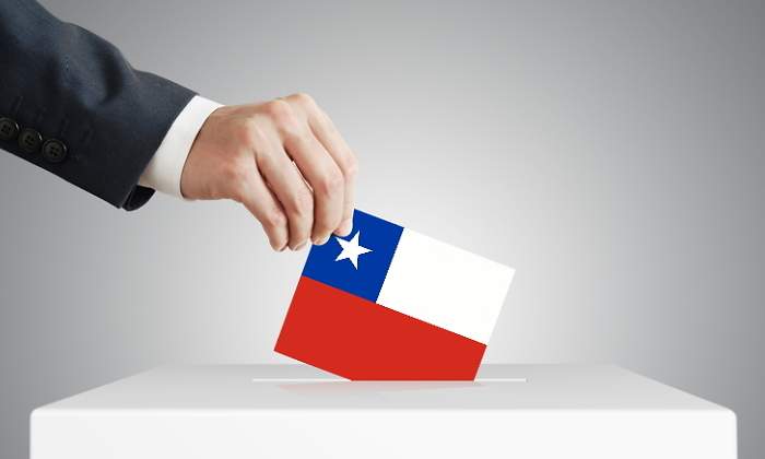 Una mano introduce un sobre con la bandera de chile en una urna