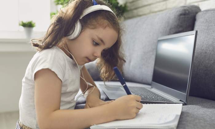 Una nia estudia en casa con auriculares y un porttil
