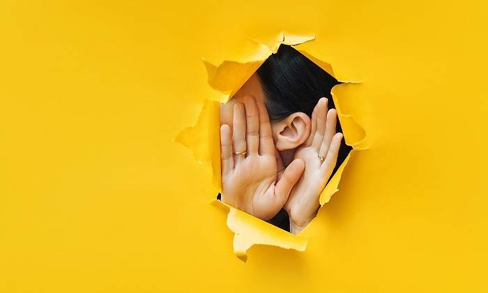 Una-mujer-mostrando-sus-manos-y-oreja-por-un-agujero-iStock.jpg