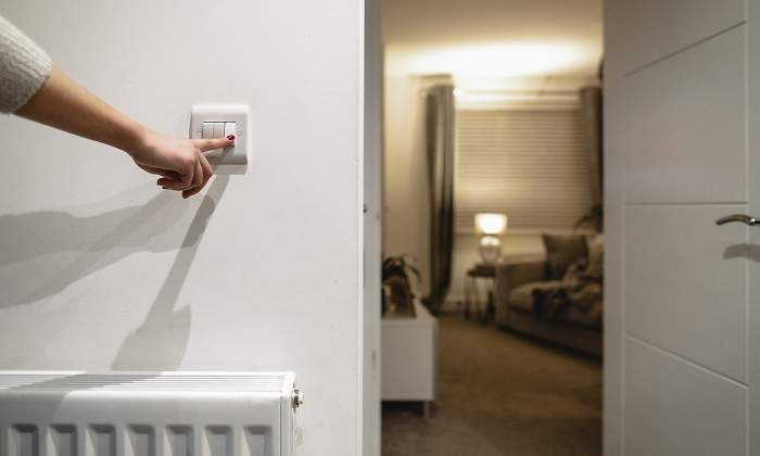 Una mano apaga un interruptor de la luz de una casa cerca de un radiador
