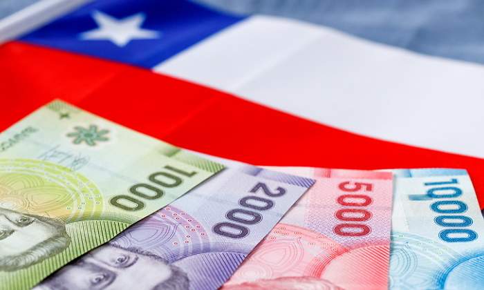 Billetes de pesos chilenos dispuestos en cantidad creciente sobre una bandera de Chile
