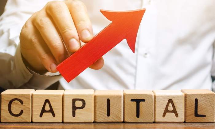 Una mano sostiene una flecha ascendente sobre letras que forman la palabra capital