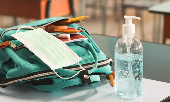 Una mochila una mascarilla y un bote de gel hidroalcohlico encima de un pupitre