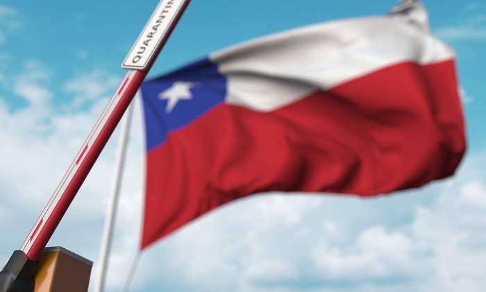 Una barrera con la palabra cuarentena se levanta con la bandera de Chile al fondo