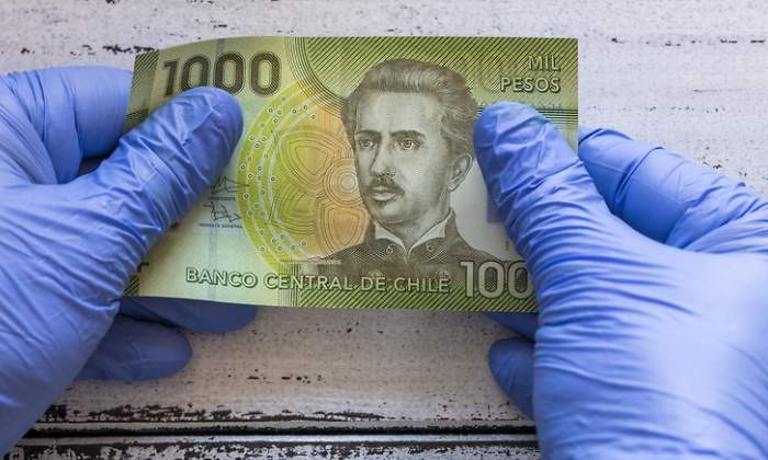Dos manos con guantes de ltex cogen un billete de mil pesos chilenos