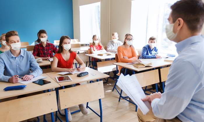 Un profesor da clase en un aula donde todos llevan mascarillas