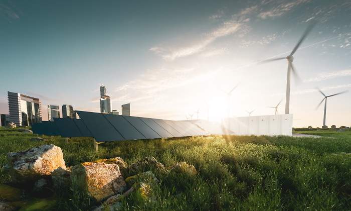 Un campo verde con placas solares y aerogeneradores con la ciudad a lo lejos
